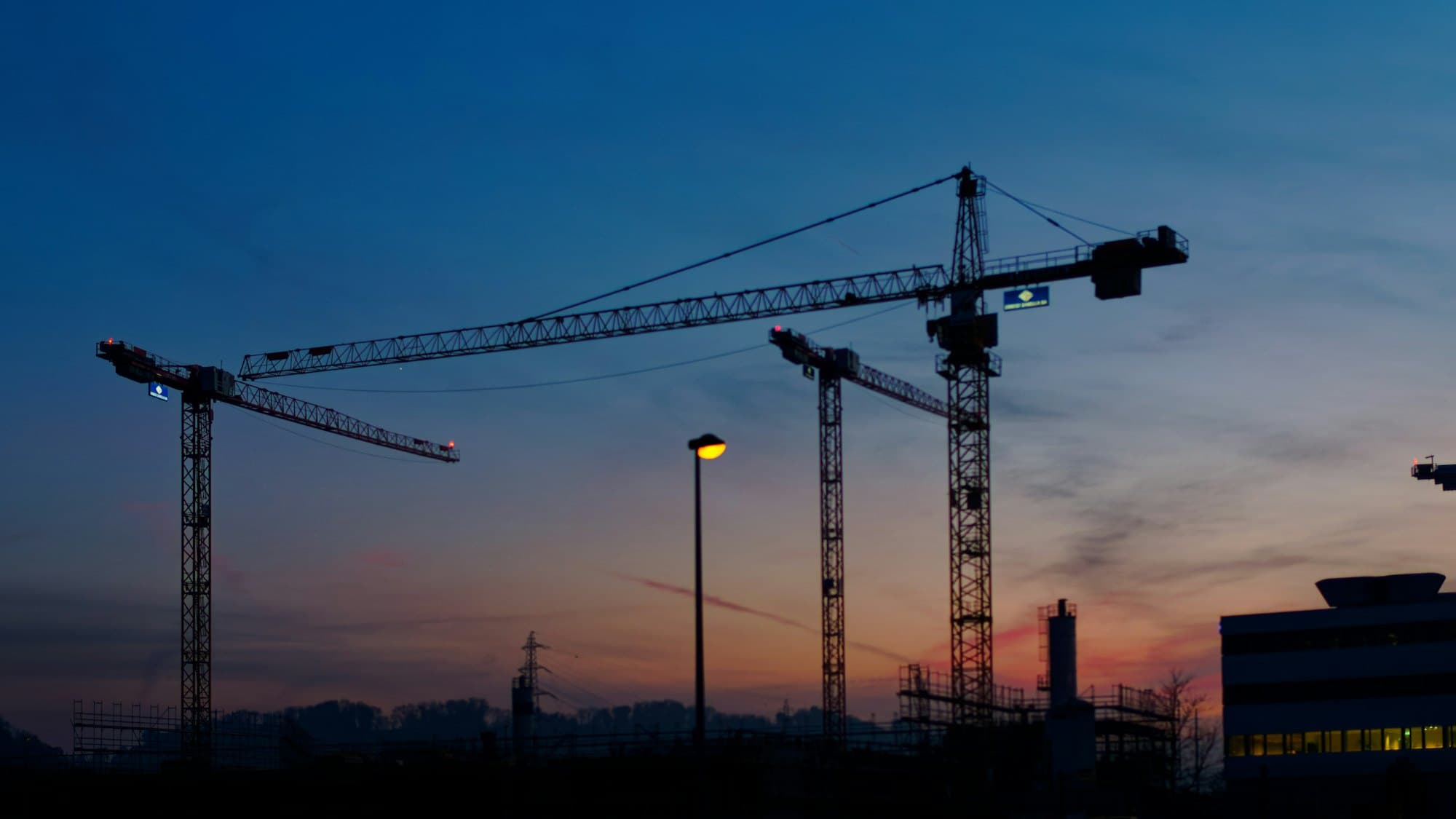 Tower cranes silhouetted against a city skyline at dusk
